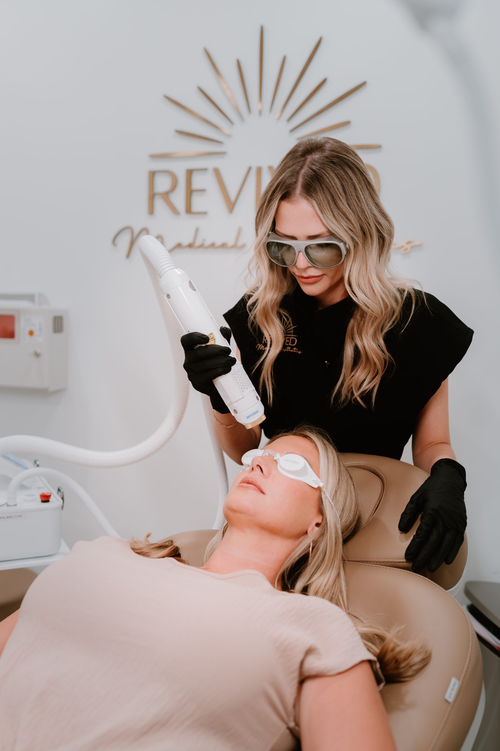 revived medical aesthetics staff performing laser treatment on patient in front of revived logo